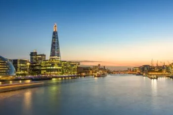 Panoramic photo of the Thames at dusk, with the Shard towering above the illuminated skyline on the left bank.