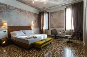 Large hotel room with patterned stone floor, two windows and large double bed
